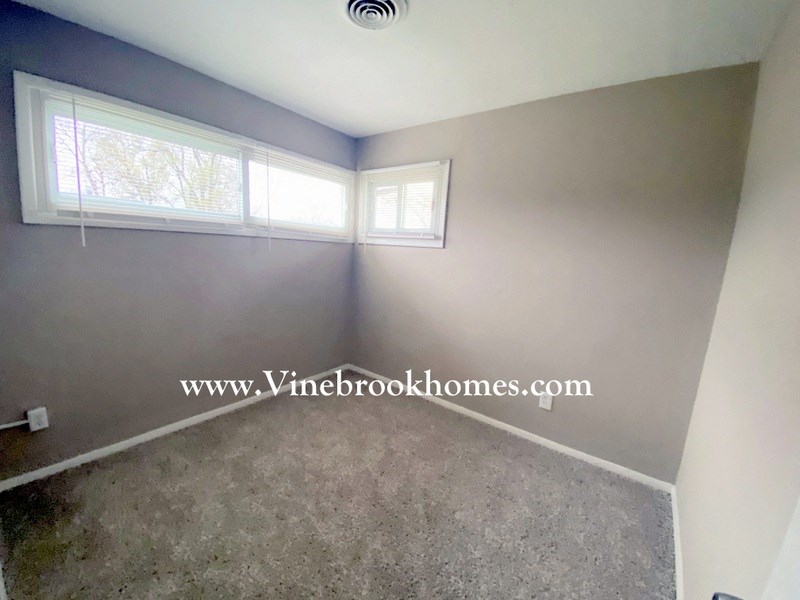 a small room with a carpet and two windows