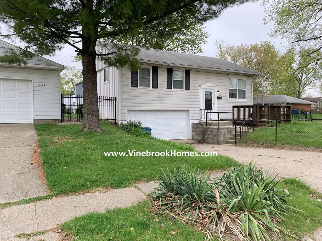 a small white house with a driveway and a tree