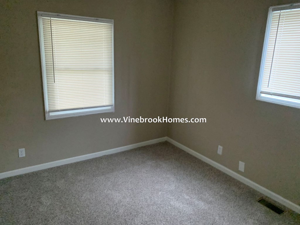 a bedroom with two windows and a carpeted floor