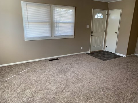 A room with a carpeted floor, two doors, and a window with blinds.