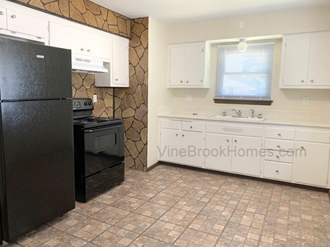 A black refrigerator sits in a kitchen with white cabinets and a tiled floor.