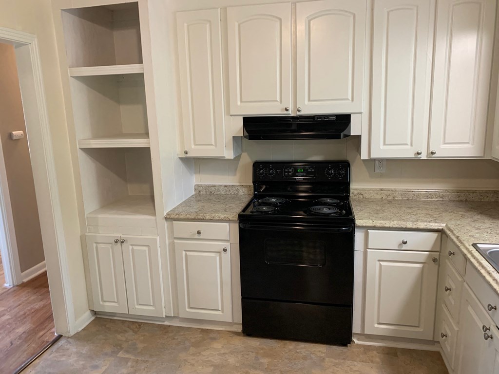 A black stove in a kitchen with white cabinets.