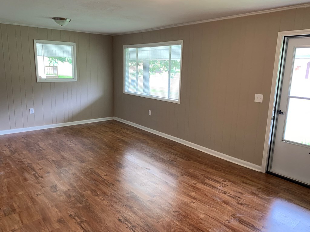 A room with wooden flooring and two windows.