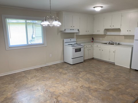 A kitchen with a white stove, white cabinets, and a window with blinds.