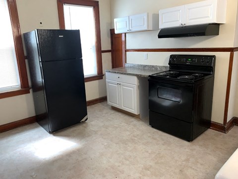 A black refrigerator stands in a kitchen with a black stove and white cabinets.