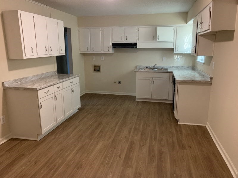 an empty kitchen with white cabinets and wooden floors