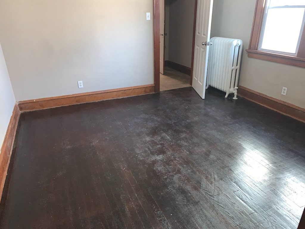 a living room with wood floors and a white wall and a radiator
