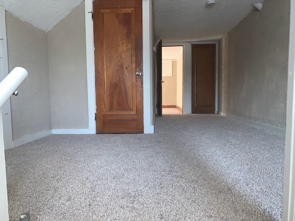 an empty living room with white carpet and a wooden door
