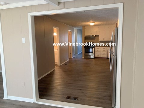 A kitchen area with a refrigerator, microwave, and cabinets is visible through an open doorway.