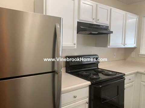 A stainless steel refrigerator stands next to a black oven in a kitchen.