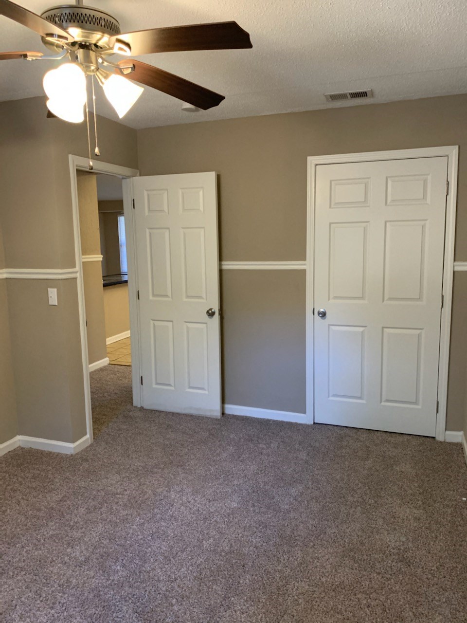an empty living room with two doors and a ceiling fan