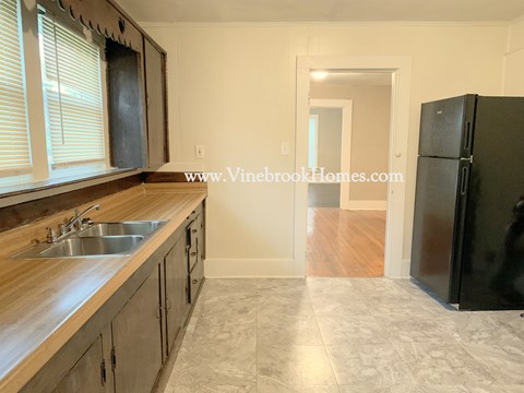 A kitchen with a sink, wooden cabinets, and a black refrigerator.