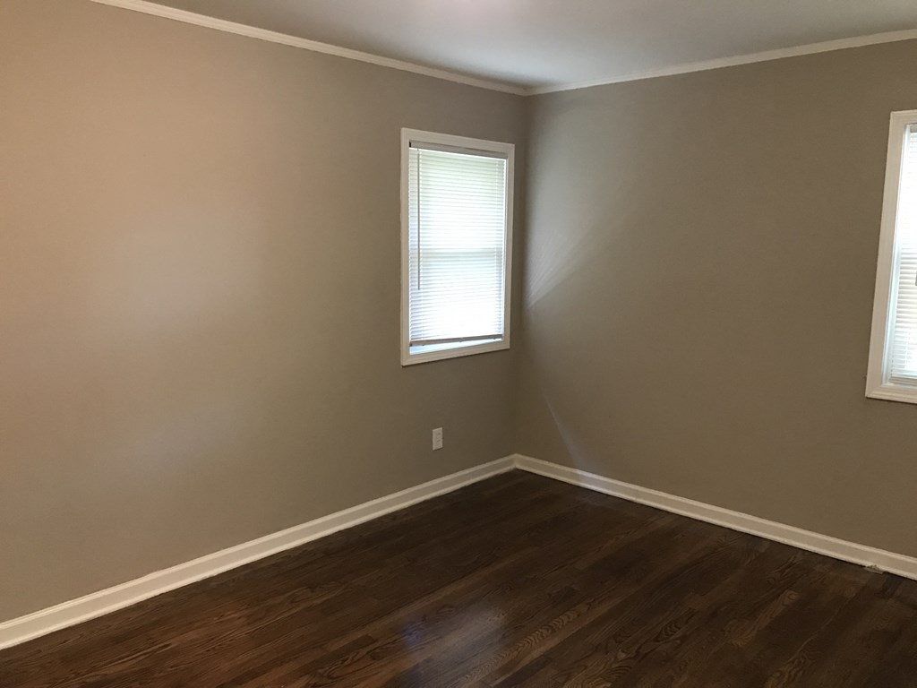 an empty room with wooden floors and two windows