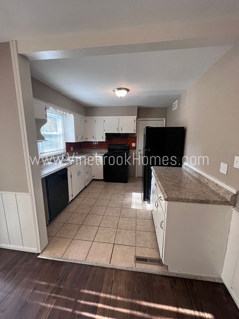 A kitchen with white cabinets and a black fridge.