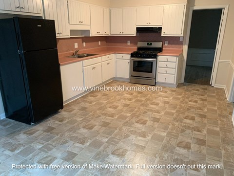 A kitchen with a black fridge, white cabinets, and a tiled floor.