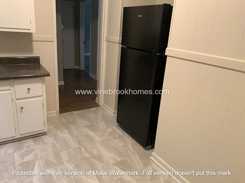 A black refrigerator in a kitchen with white cabinets and a tiled floor.