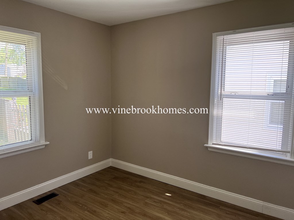 a corner of a room with two windows and a wooden floor