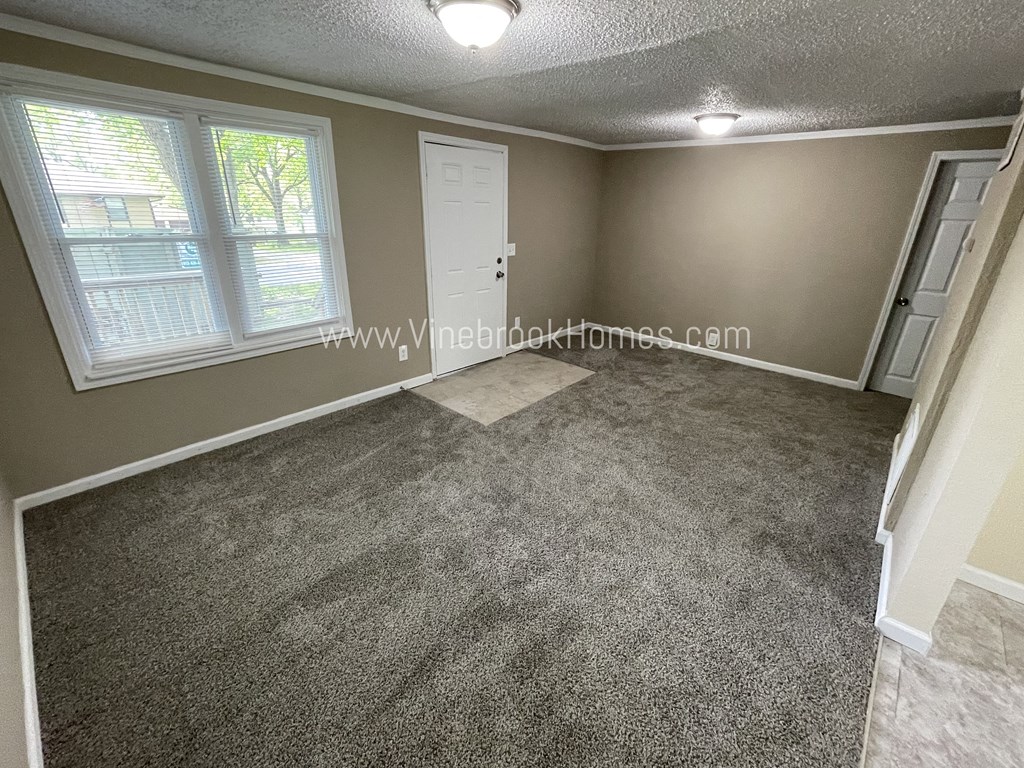 a small carpeted living room with a white door and two windows
