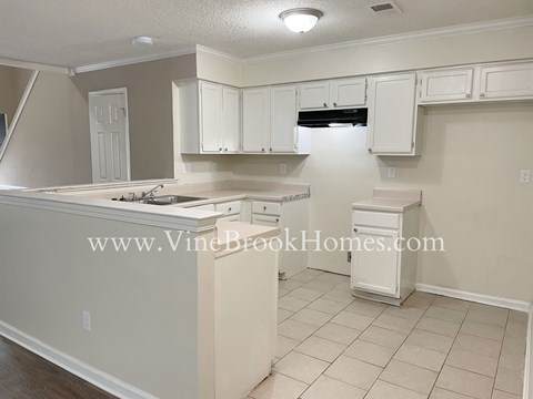 A kitchen with white cabinets and a website address on the wall.