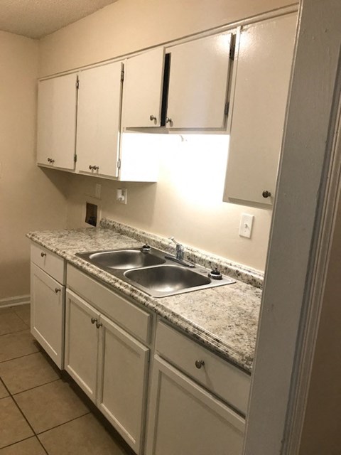 A kitchen with a granite counter top and white cabinets.
