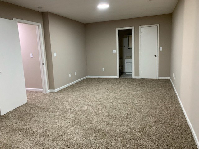 an empty room with carpet and a door to a bathroom