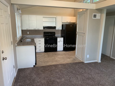 A kitchen with white cabinets and a black fridge.