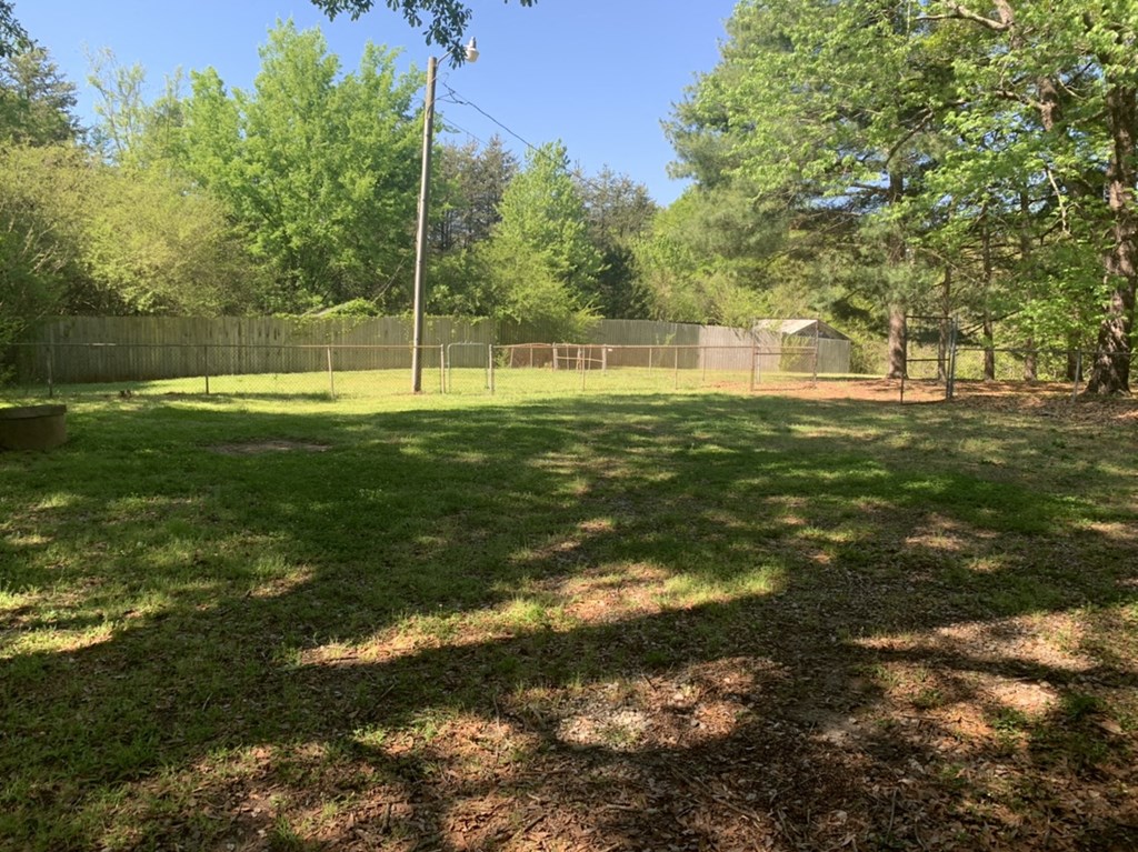 the backyard of the home has a fenced in area with grass and trees