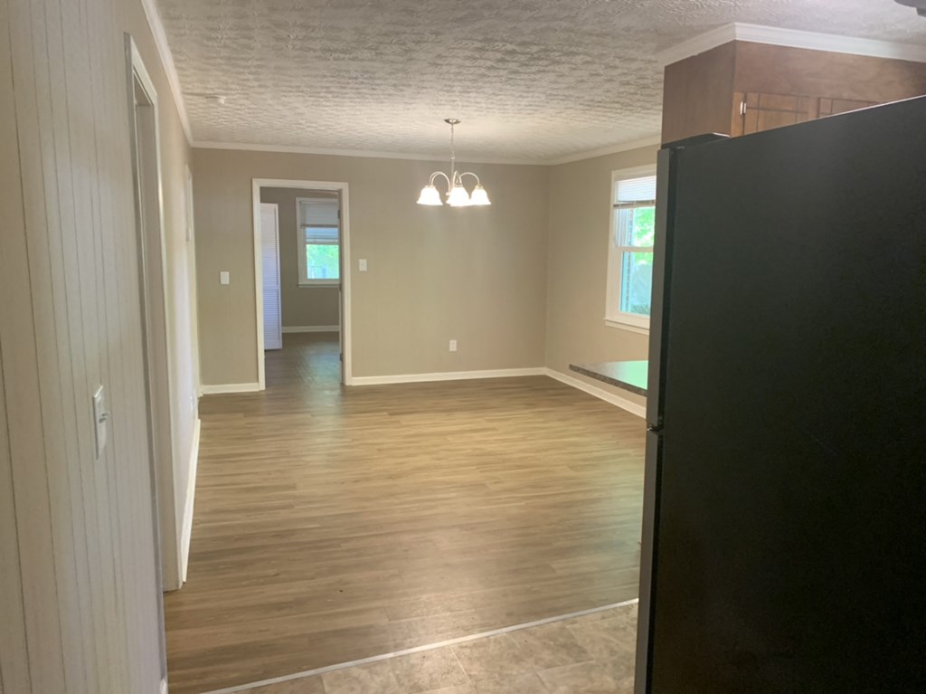 an empty living room with wooden floors and a black refrigerator