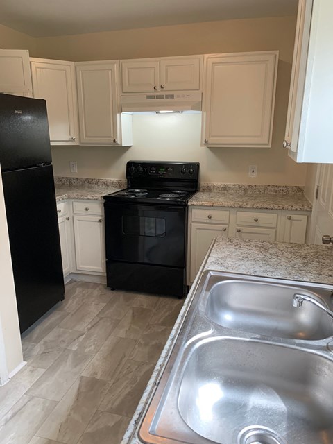 A black refrigerator is in a kitchen with a stove and sink.