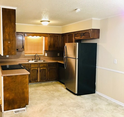 A kitchen with a black refrigerator and wooden cabinets.