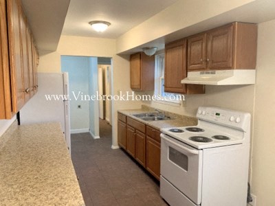 A kitchen with a white stove top oven and wooden cabinets.
