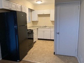 A black refrigerator in a kitchen with white cabinets.