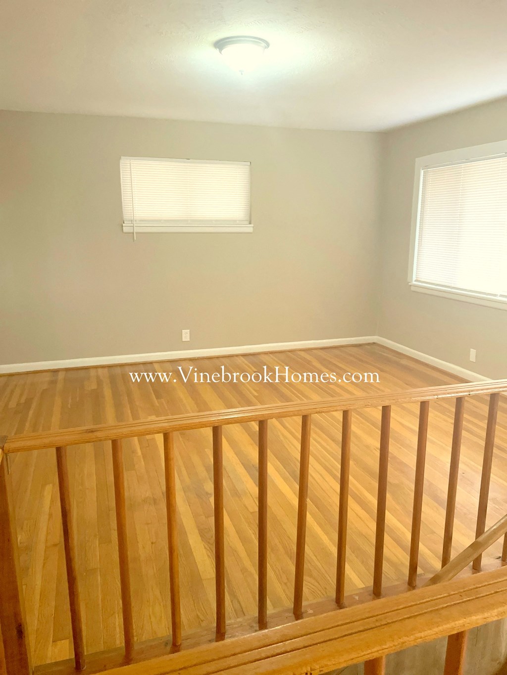 the top of a wooden railing in a room with two windows