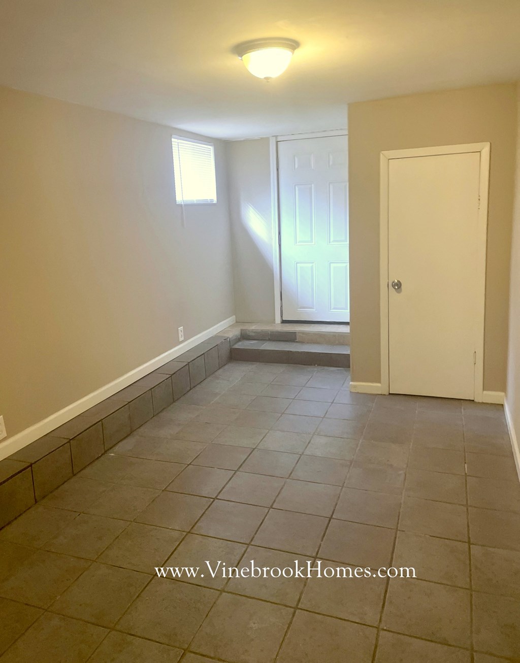 an empty living room with a tile floor and a white door