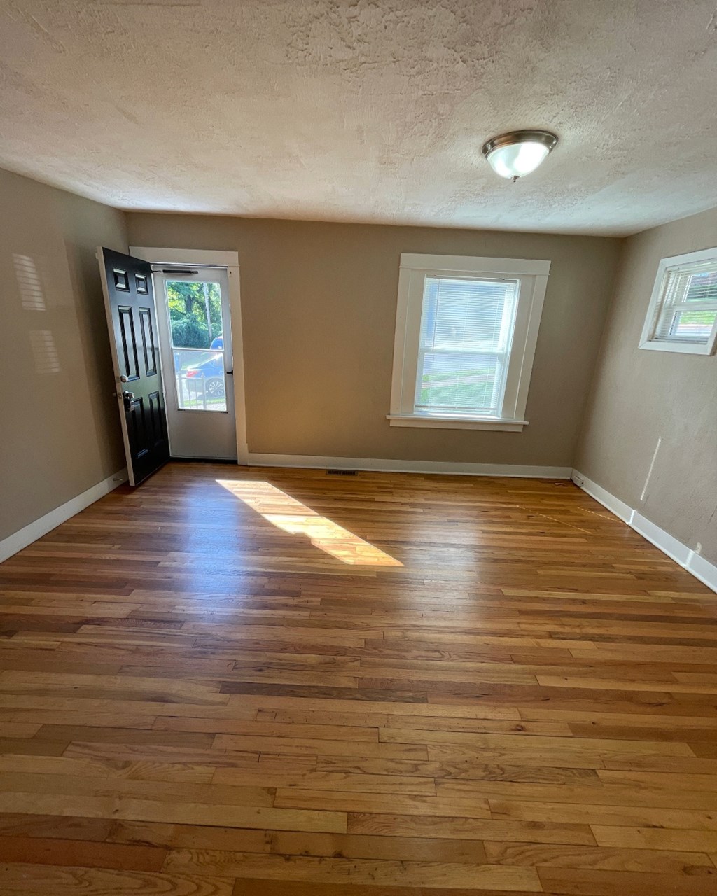 an empty living room with wooden floors and a door to a house