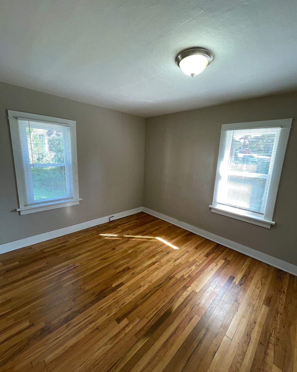 an empty room with wooden floors and two windows