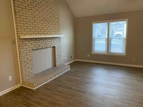 an empty living room with a brick fireplace and wooden floors