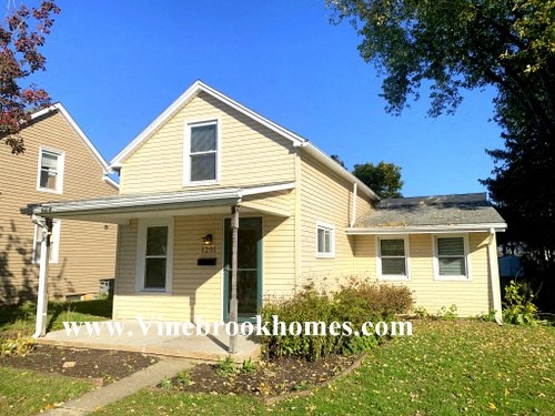 a yellow house with a covered porch and a tree