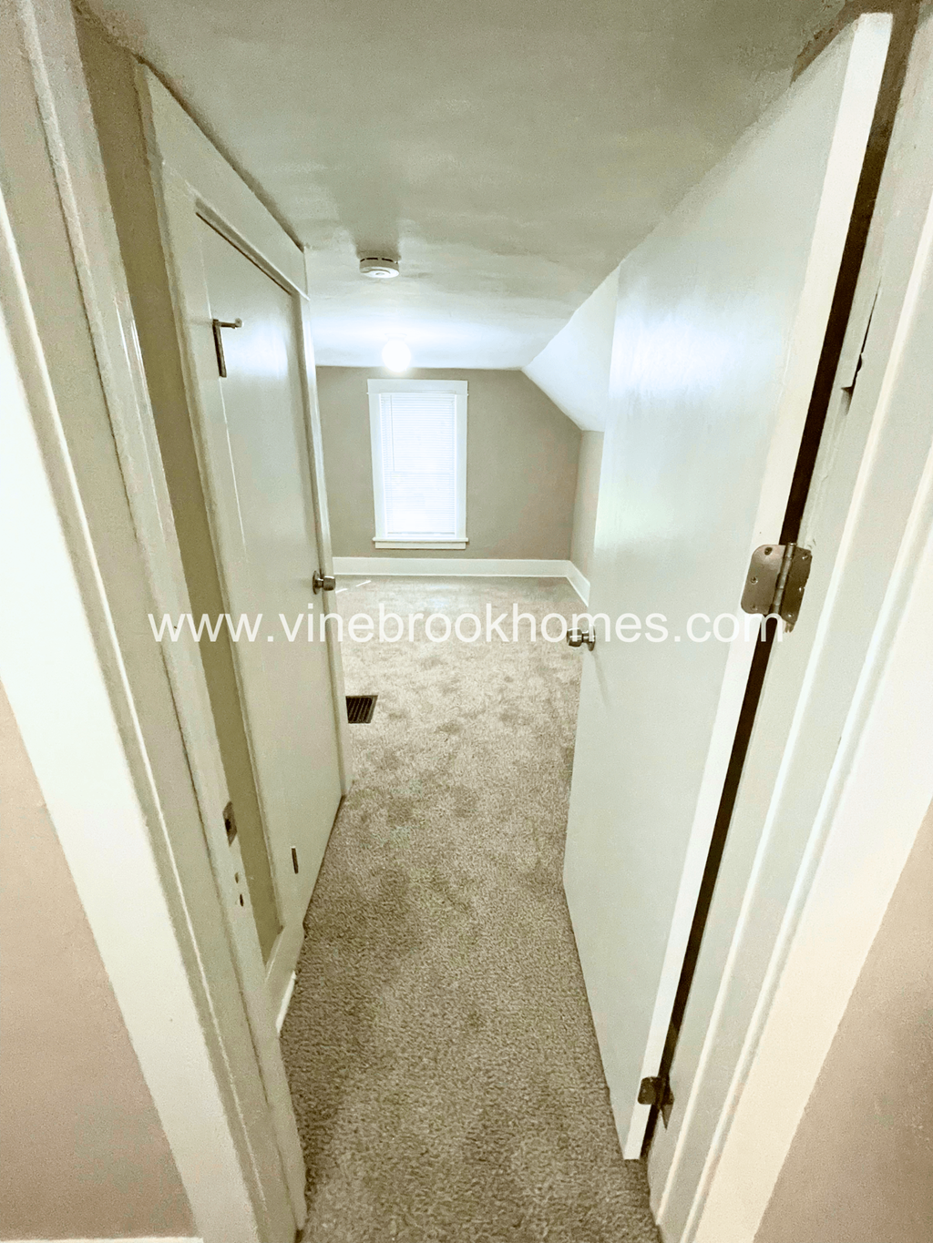 a narrow hallway with a door to a closet and a window