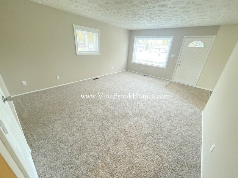 a white carpeted living room with a white door and a window