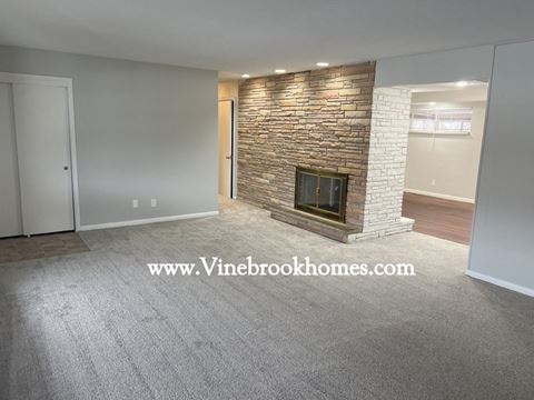 a living room with a stone fireplace and gray carpet