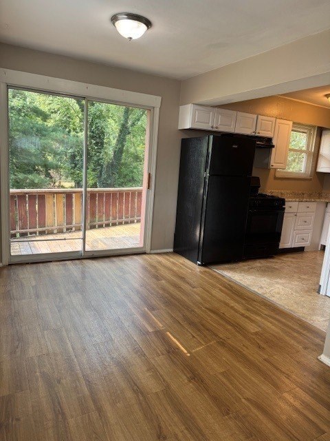 A black refrigerator sits in a kitchen with wooden floors and a balcony outside.