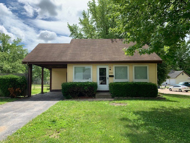 a small yellow house with a driveway and a tree