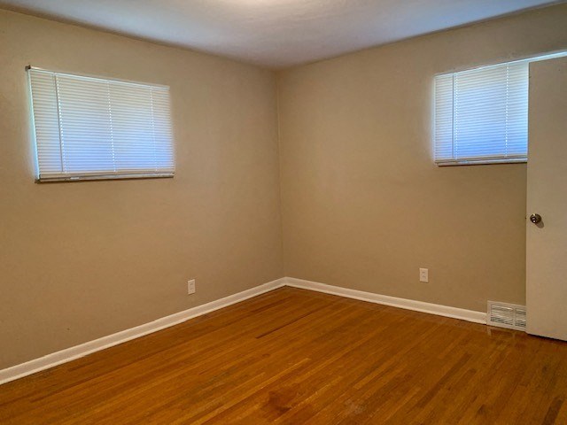 an empty room with a wooden floor and two windows
