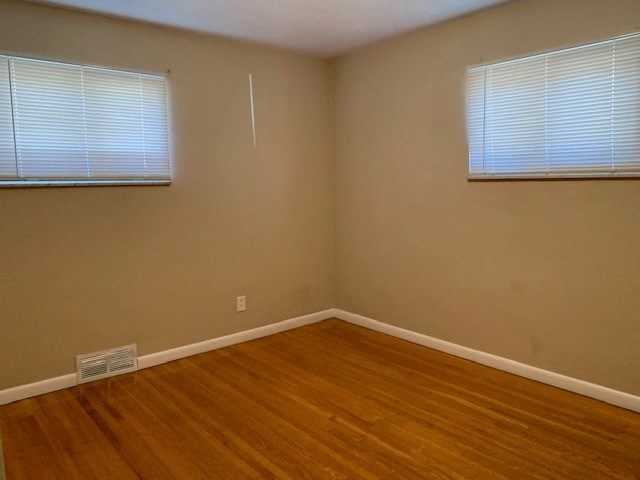 an empty room with a wooden floor and two windows