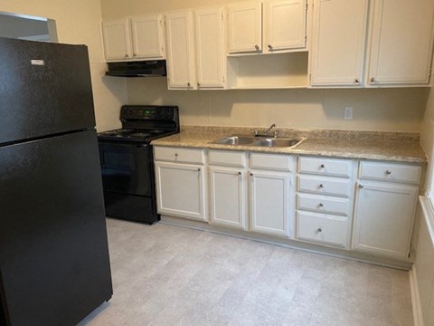 A black refrigerator is in a kitchen with white cabinets.