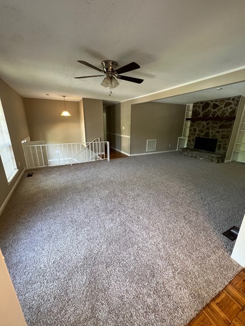 A living room with a grey carpet and a ceiling fan.