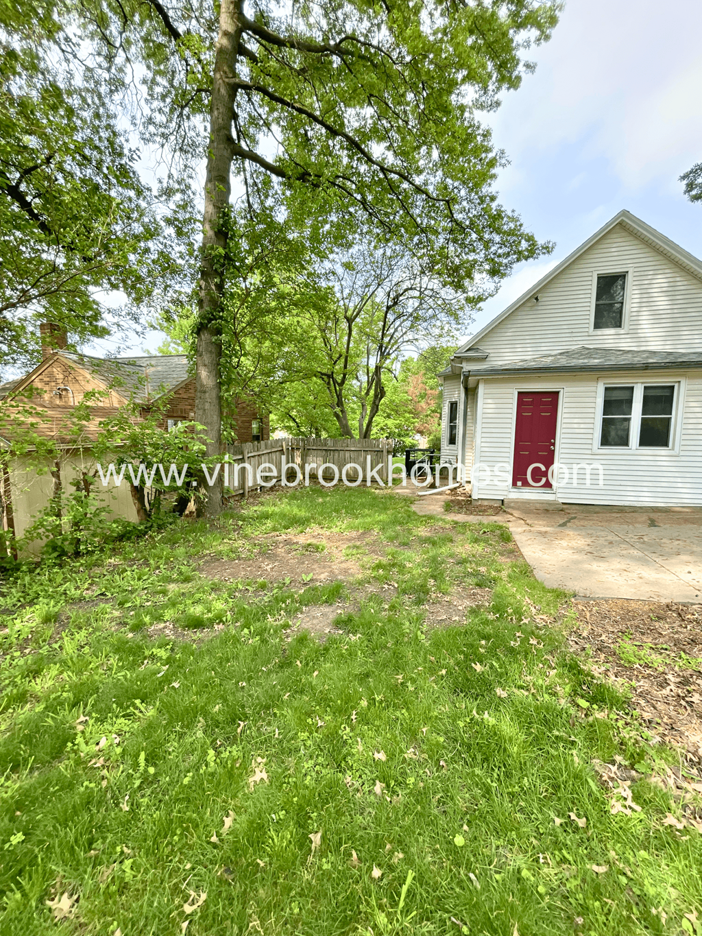 a small white house with a red door and grass and trees