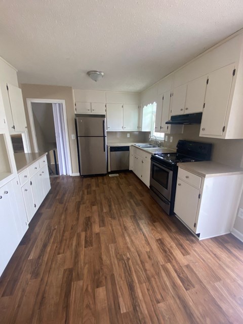 A kitchen with white cabinets and wooden floors.