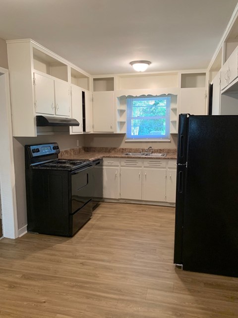 A black refrigerator is on the right in a kitchen with white cabinets.
